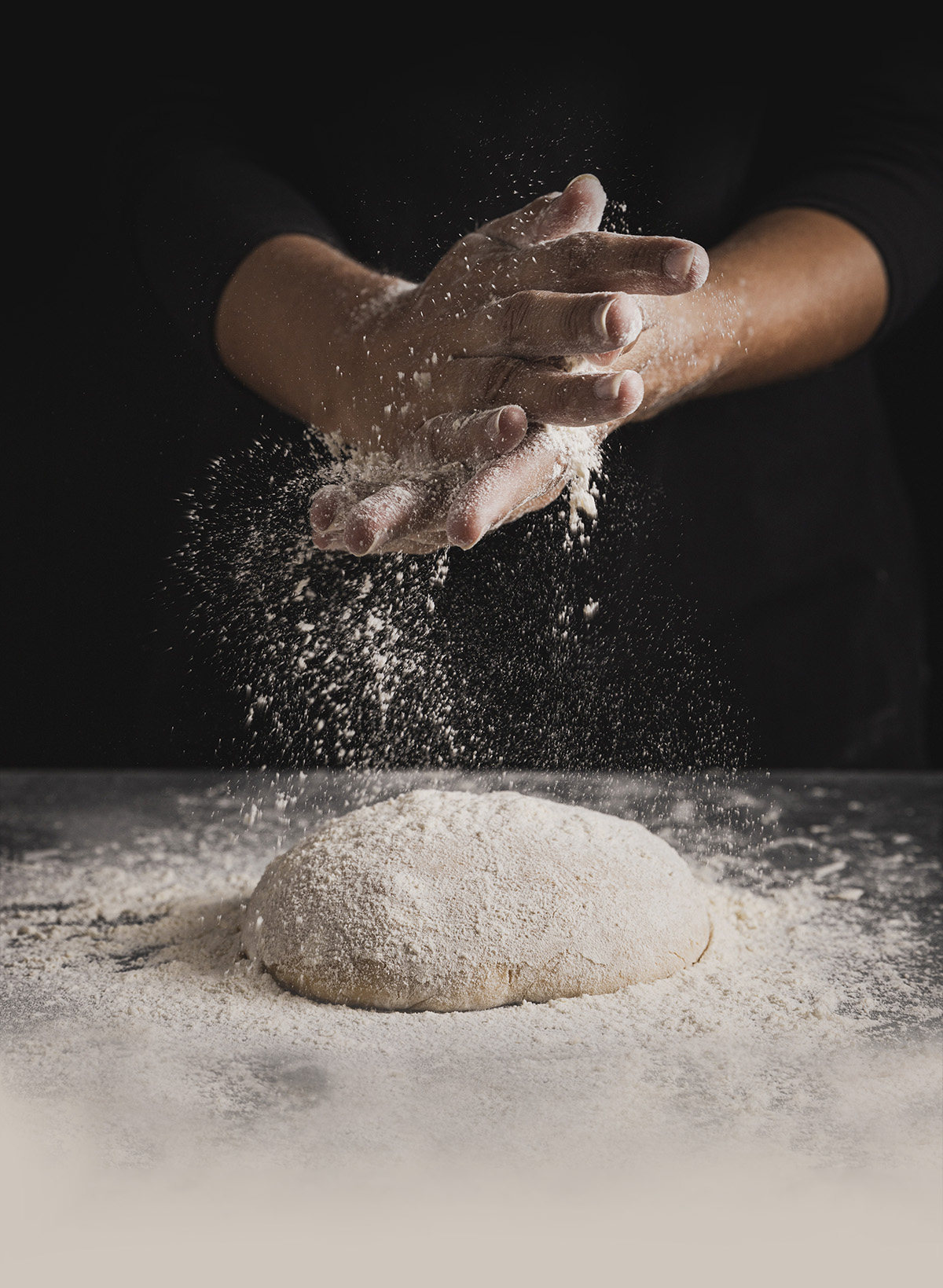 Pizzabagares händer häller mjöl över en pizzadeg